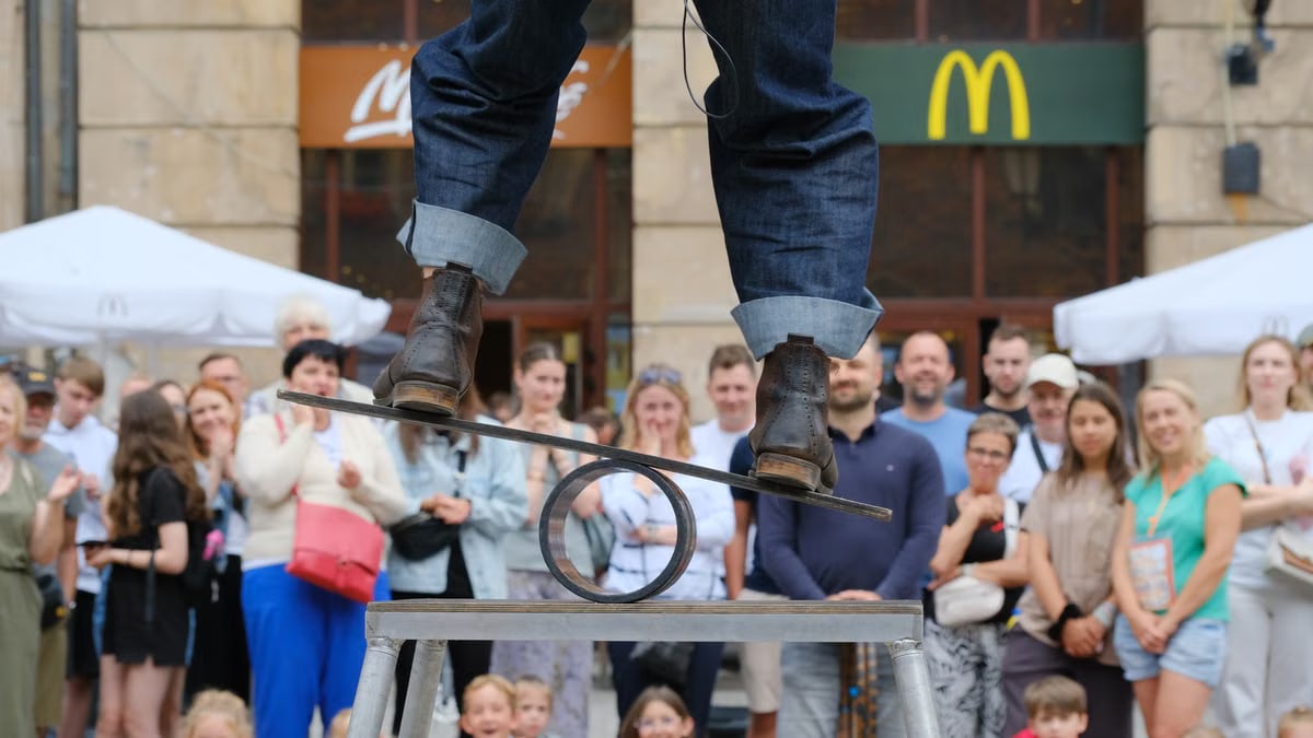 A street performer skillfully balances on a metal structure, captivating a crowd in an urban setting.