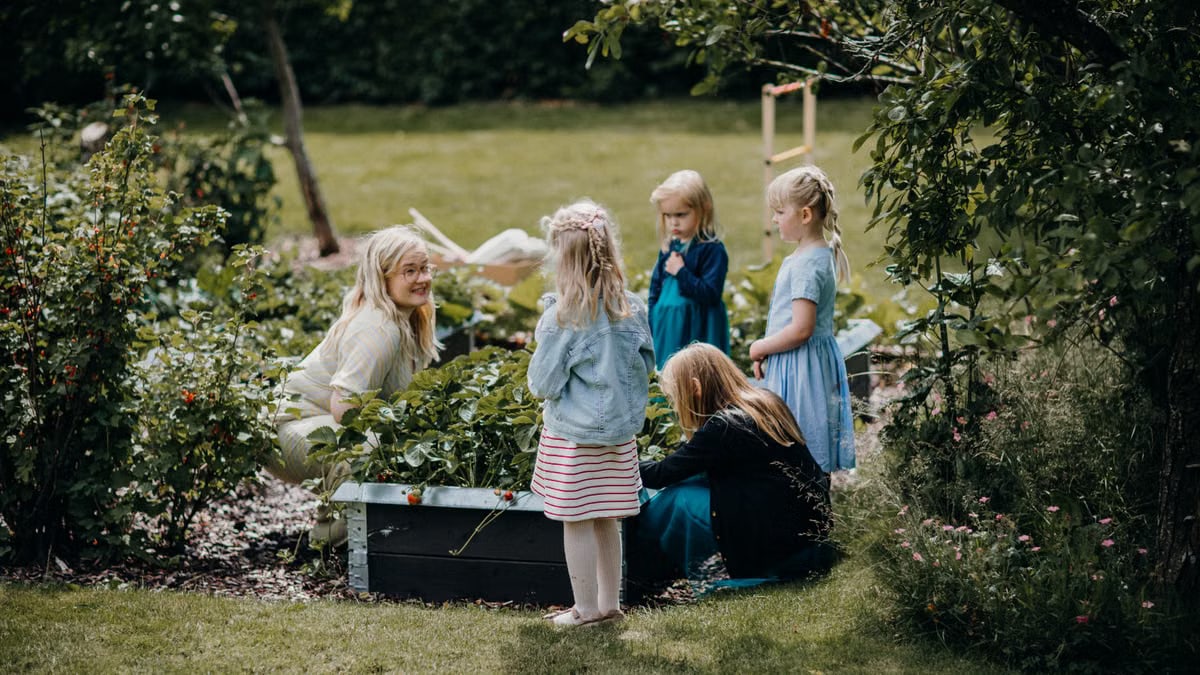 A group of children and an adult gardening together in a lush, green backyard setting, enjoying outdoor activities.